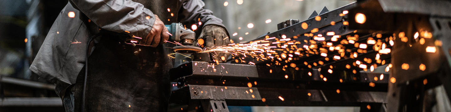 Acciaio laminato a caldo in lavorazione: il metallo brilla sotto le scintille e mostra una finitura grezza ma resistente, pronta
