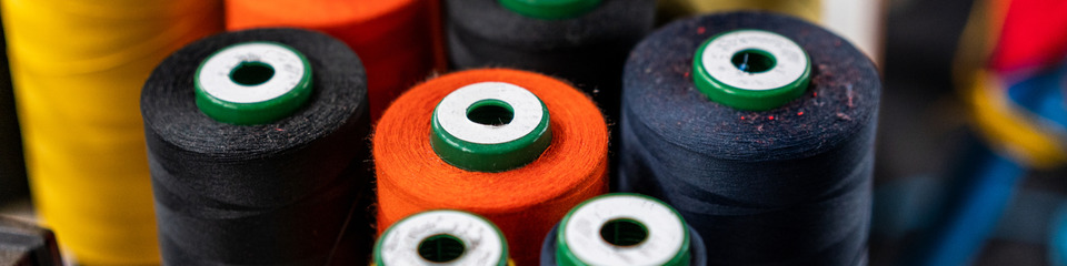 I fili di cotone, disposti ordinatamente su scaffali, brillano sotto la luce calda del laboratorio di cucito.