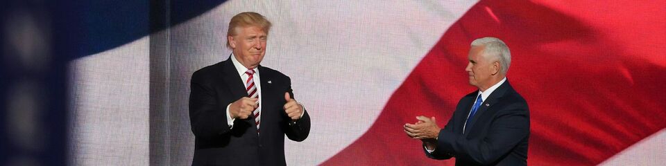 Trump sul palco con aria vincente, come sfondo la bandiera americana