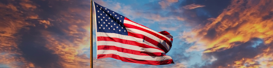 Usa_websim15 Una bandiera a stelle e strisce che danza al vento su un molo affollato, mentre il sole tramonta all'orizzonte