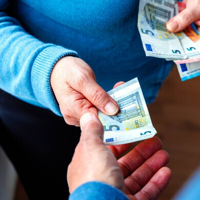 Inquadratura oltre la spalla di una donna che consegna una banconota da cinque euro a un uomo