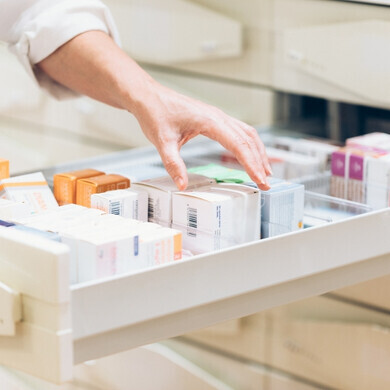 Mano di una farmacista che preleva medicinali da un cassetto in farmacia, simbolo di cura e gestione dei farmaci.