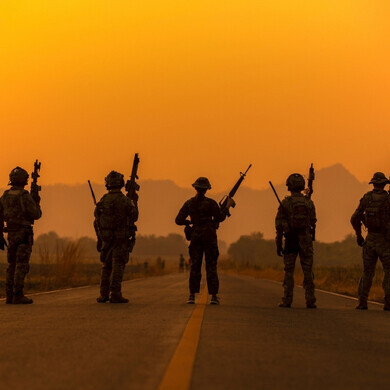 Sagome di soldati sullo sfondo del cielo al tramonto Sagome di soldati in azione sullo sfondo di un cielo arancione al tramonto, simbolo di esercito e operazioni militari.