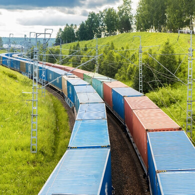 Fotografia di un convoglio di vagoni merci in movimento su rotaie, con locomotiva visibile in testa.