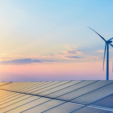 Campo di pale eoliche e pannelli fotovoltaici sotto un cielo arancione all’alba