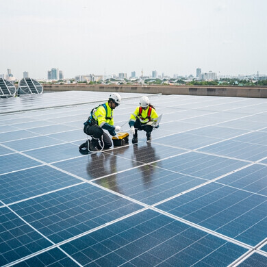 Tecnici uomo e donna con giubbotti riflettenti e caschi installano pannelli solari in una giornata di sole, utilizzando laptop e voltmetro Un uomo e una donna, entrambi con giubbotti fluorescenti e caschi di sicurezza, installano pannelli solari in una giornata soleggiata utilizzando laptop e voltmetro.