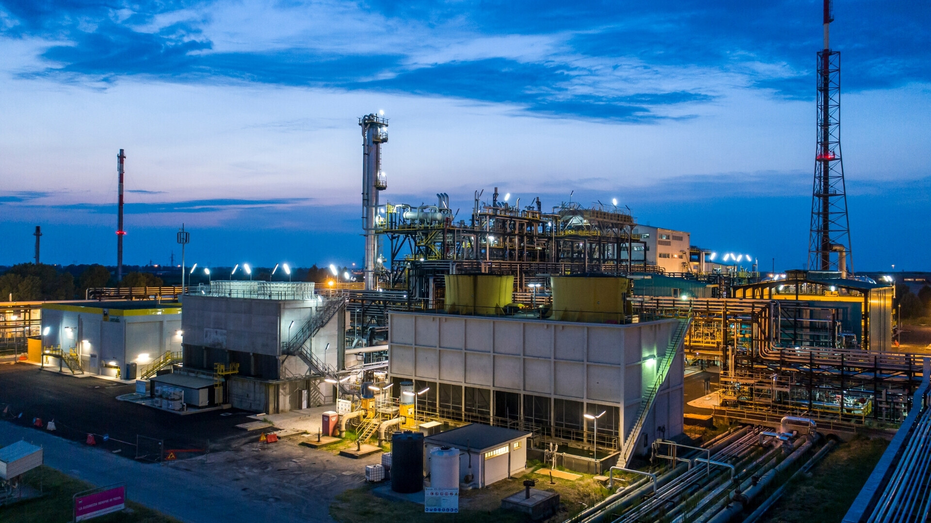 Raffineria industriale gestita da Saipem, con torri di distillazione e impianti di processo visibili.