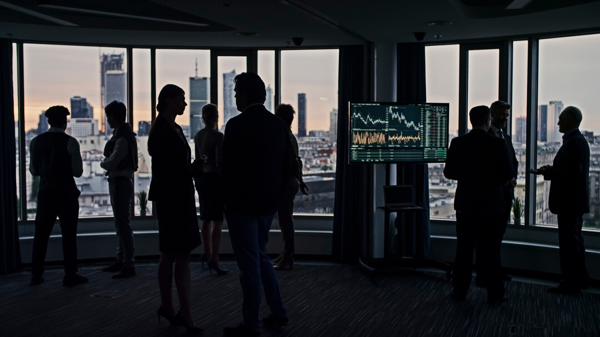 Gli uomini d'affari si distogliano alle finestre dei grattacieli. Analisi del trading azionario sullo schermo Persone d’affari di diverse etnie che camminano e discutono della situazione del mercato azionario, silhouette scure.