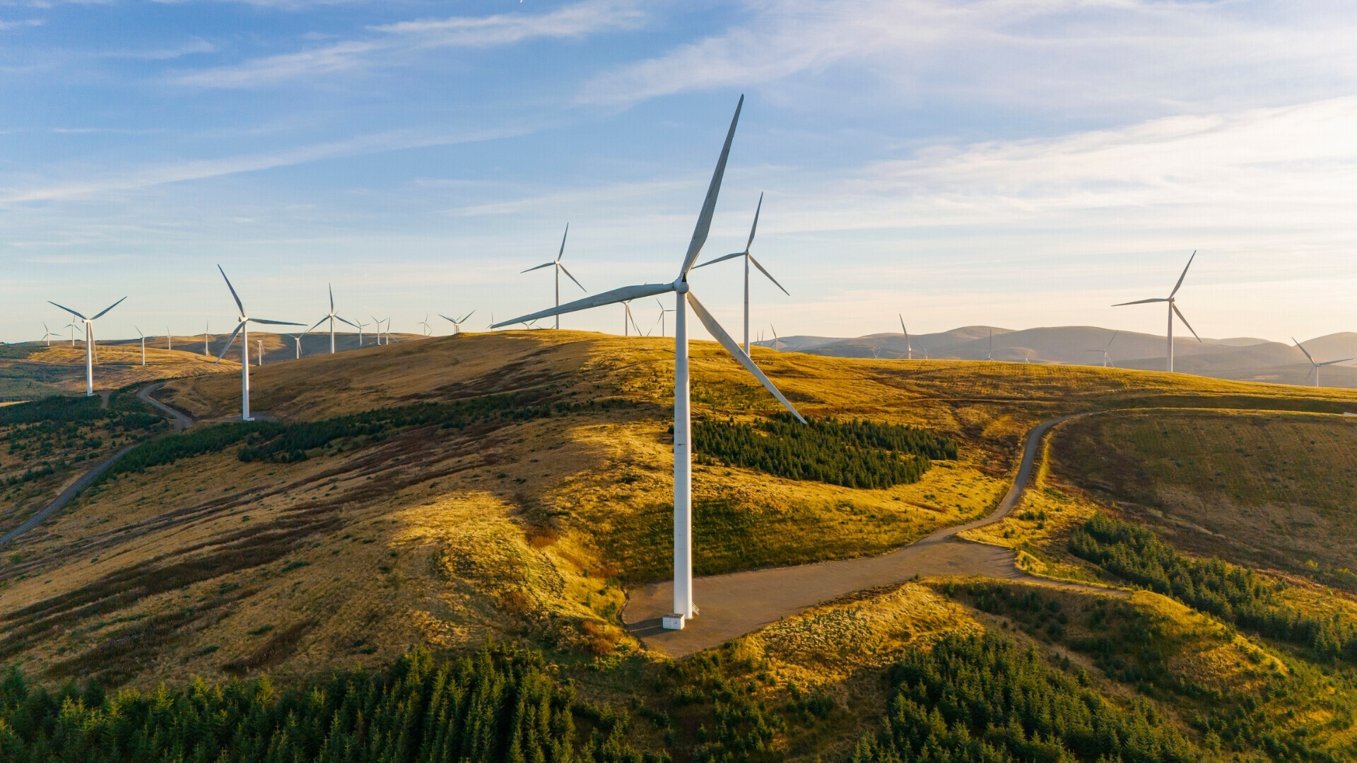 Vista aerea/droni di un parco eolico su una collina in Scozia Veduta aerea di un parco eolico su una collina scozzese, con numerose turbine che sfruttano l’energia del vento in un paesaggio verde e ondulato.