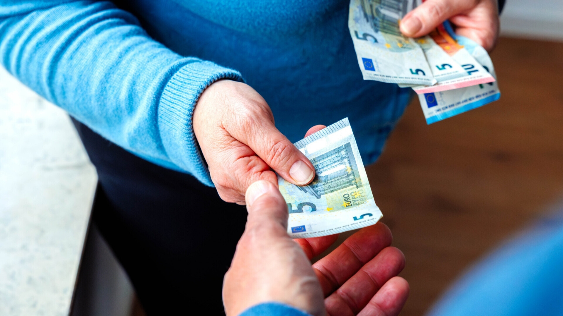 Inquadratura oltre la spalla di una donna che consegna una banconota da cinque euro a un uomo