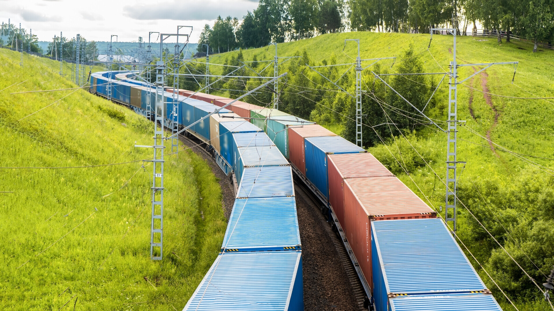 Treno merci Fotografia di un convoglio di vagoni merci in movimento su rotaie, con locomotiva visibile in testa.