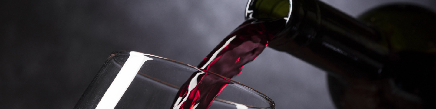 Mani esperte che versano vino rosso in un bicchiere cristallino